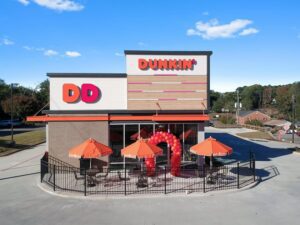 Front of new Dunkin' Donut's building with Honey Glaze siding, blue skies, balloon arch and orange Dunkin' Donut's umbrellas